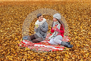 Adorable teens communicate drink tea talk while sitting in a park on a plaid picnic