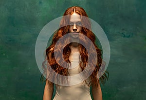 Adorable tender redhead girl with long curly hair  over dark green background. Fabolous curly hair and harming