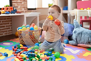 Adorable toddler bitting ball sitting on floor at kindergarten