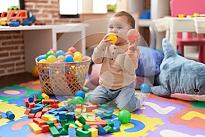 Adorable toddler bitting ball sitting on floor at kindergarten