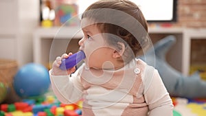 Adorable toddler bitting plastic food toy sitting on floor at kindergarten