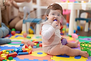 Adorable toddler bitting plastic food toy sitting on floor at kindergarten