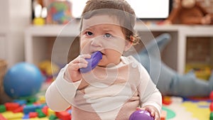 Adorable toddler bitting plastic food toy sitting on floor at kindergarten