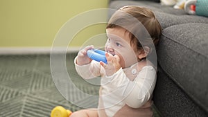 Adorable toddler bitting plastic hoop sitting on floor at home