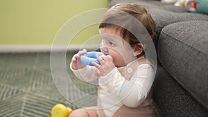 Adorable toddler bitting plastic hoop sitting on floor at home