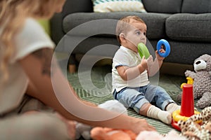 Adorable toddler bitting plastic hoop sitting on floor at home