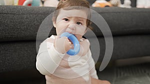 Adorable toddler bitting plastic hoop sitting on floor at home