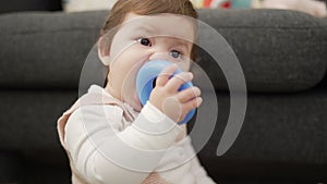 Adorable toddler bitting plastic hoop sitting on floor at home