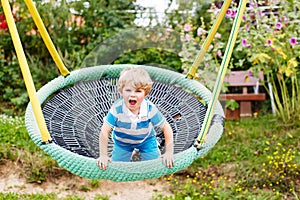 Adorable toddler boy having fun chain swing on outdoor playgroun