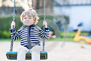 Adorable toddler boy having fun chain swing on outdoor playground