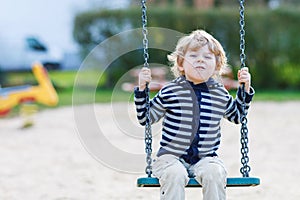 Adorable toddler boy having fun chain swing on outdoor playground