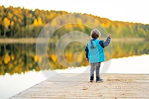 Adorable toddler boy having fun by the Gela lake on sunny fall day. Child exploring nature on autumn day in Vilnius, Lithuania