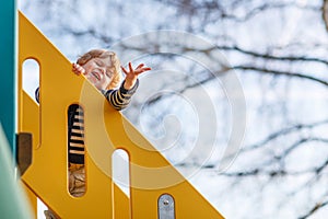 Adorable toddler boy having fun and sliding on outdoor playground