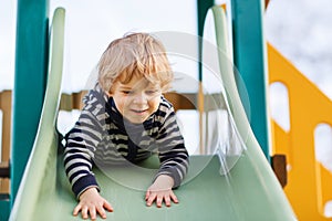 Adorable toddler boy having fun and sliding on outdoor playground
