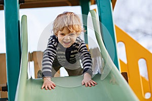Adorable toddler boy having fun and sliding on outdoor playground