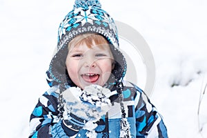 Adorable toddler boy having fun with snow on winter day