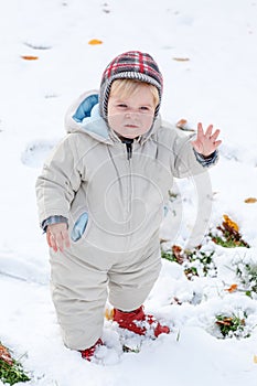 Adorable toddler boy having fun with snow on winter day