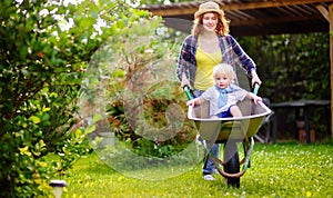 Adorable toddler boy having fun in a wheelbarrow pushing by mum