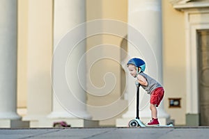 Adorable toddler boy riding his scooter in a city on sunny summer evening. Young child riding a roller