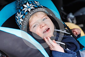 Adorable toddler boy sitting in safety car seat