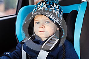 Adorable toddler boy sitting in safety car seat