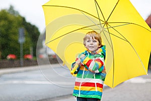 Adorable toddler boy with yellow umbrella and colorful jacket outdoors at rainy day