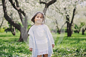 Adorable toddler child girl in light blue dressy outfit walking and playing in blooming spring garden
