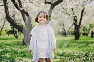 Adorable toddler child girl in light blue dressy outfit walking and playing in blooming spring garden