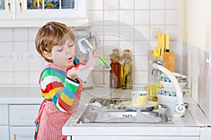 Adorable toddler child washing dishes in domestic kitchen.
