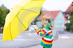 Adorable toddler child with yellow umbrella and colorful jacket