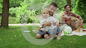 Adorable toddler falling on grass in park. Parents laughing with kids outdoors