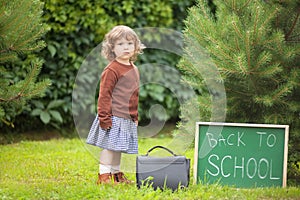 Adorable toddler girl; back to school written on chalk blackboard