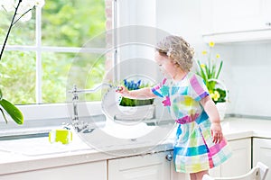 Adorable toddler girl in colorful dress washing dishes