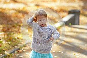 Adorable toddler girl dancing in the park on a beautiful sunny autumn day.