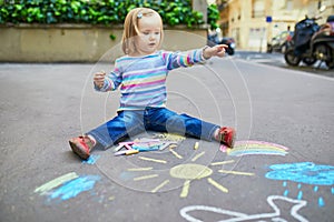 Adorable toddler girl drawing with colorful chalks on asphalt