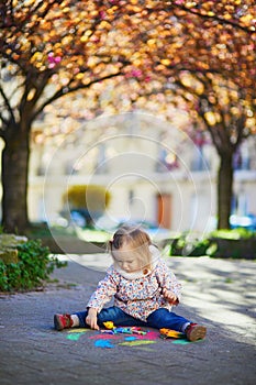 Adorable toddler girl drawing with colorful chalks on asphalt