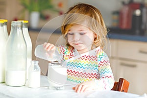 Adorable toddler girl drinking cow milk for breakfast. Cute baby daughter with lots of bottles. Healthy child having