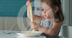 Adorable toddler girl eat pasta spaghetti, happy preschool child eating, girl shoving pasta in her mouth with her hands