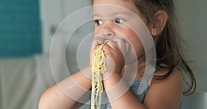 Adorable toddler girl eat pasta spaghetti, happy preschool child eating, girl shoving pasta in her mouth with her hands