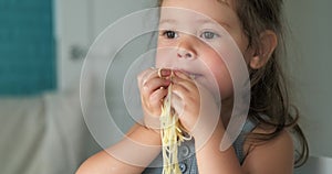 Adorable toddler girl eat pasta spaghetti, happy preschool child eating, girl shoving pasta in her mouth with her hands