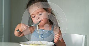 Adorable toddler girl eat pasta spaghetti, happy preschool child eating using fork and by hands fresh cooked healthy