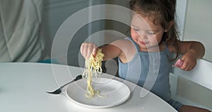 Adorable toddler girl eat pasta spaghetti, happy preschool child eating using fork and by hands fresh cooked healthy