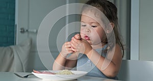 Adorable toddler girl eat sausage with pasta spaghetti, happy preschool child eating using fork and by hands fresh