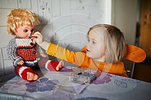 Adorable toddler girl eating blueberries and feeding her doll