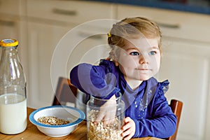 Adorable toddler girl eating healthy oatmeals with milk for breakfast. Cute happy baby child in colorful clothes sitting