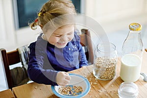 Adorable toddler girl eating healthy oatmeals with milk for breakfast. Cute happy baby child in colorful clothes sitting