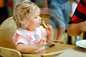 Adorable toddler girl eating healthy vegetables and unhealthy french fries potatoes. Cute happy baby child taking food