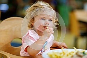 Adorable toddler girl eating healthy vegetables and unhealthy french fries potatoes. Cute happy baby child taking food