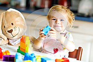 Adorable toddler girl with favorite plush bunny playing with educational toys in nursery. Happy healthy child having fun
