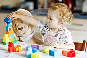 Adorable toddler girl with favorite plush bunny playing with educational toys in nursery. Happy healthy child having fun
